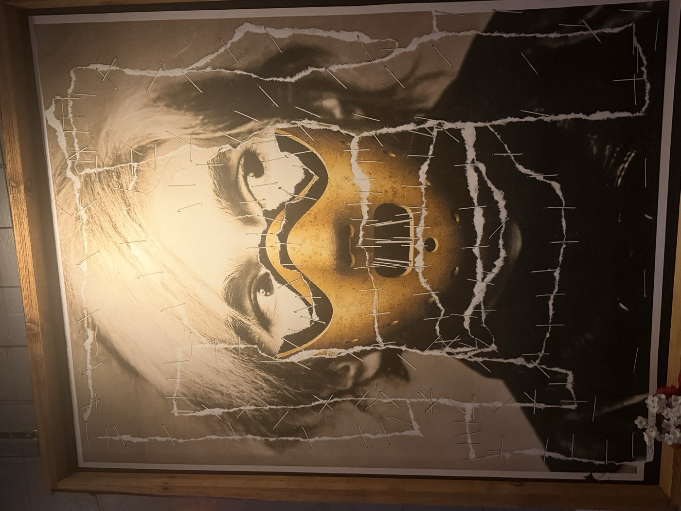 Framed stapled collage: a gold restraint mask torn across a silver-screen portrait