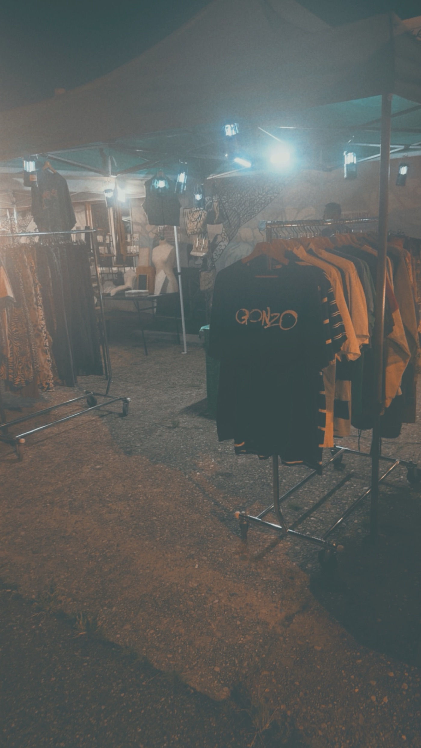Rack of tees under string lights with mannequins behind